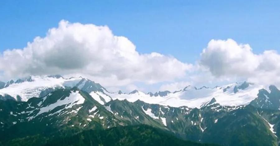 The whole Olympus massif with snow on the high peaks under white clouds