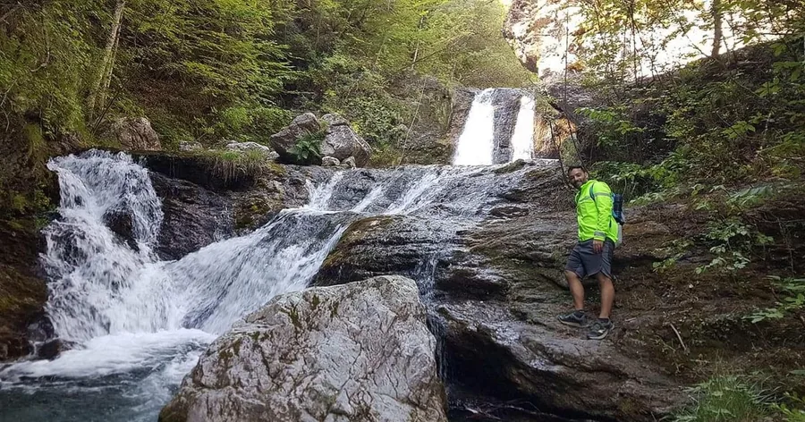 A hiker beside a mountain stream cascading over rocks in the forest