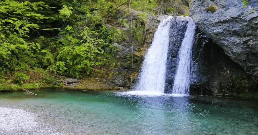 A waterfall pouring into a clear green pool in the foothills